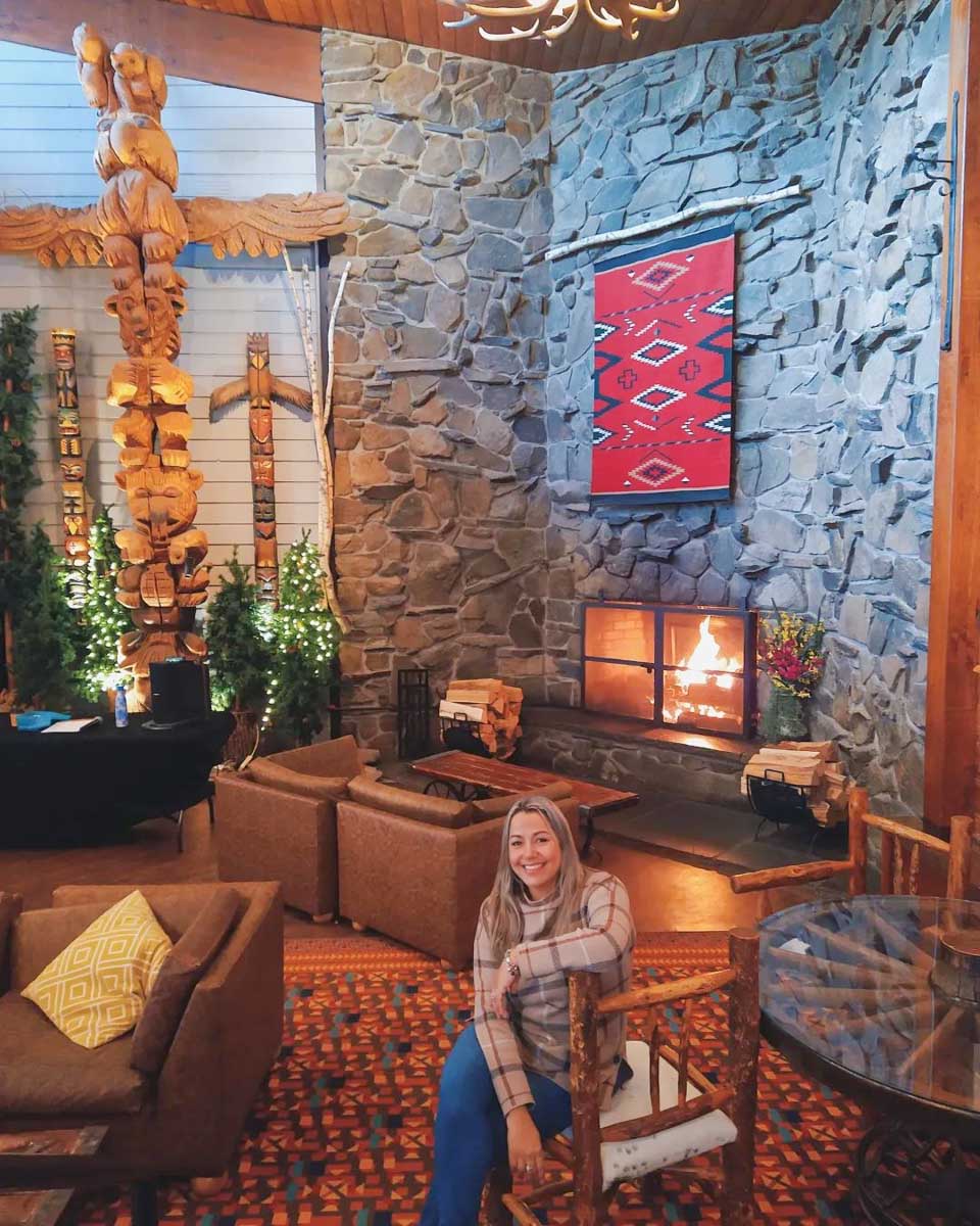 A woman sitting on a chair inside a room in Rocking Horse Ranch Resort with a fireplace in the background.